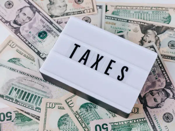 This is a white box with the word "TAXES" that's on a pile of dollar bills